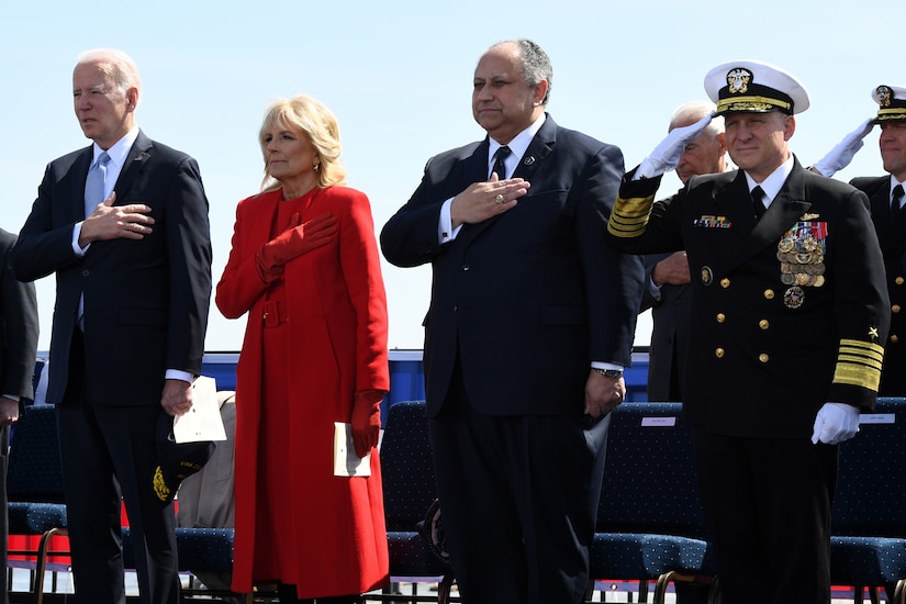 Three men and a woman stand with their hands over their hearts.