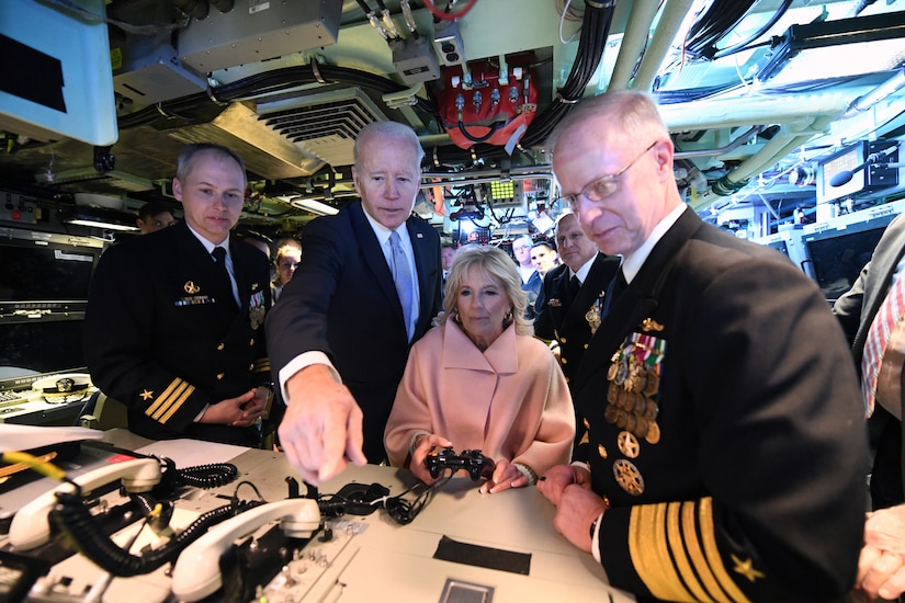 Three men and a woman look at a counter of phones and wires.