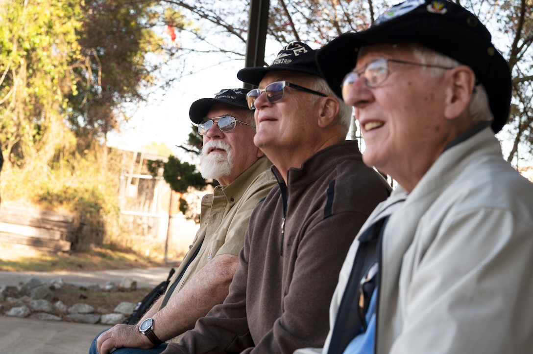 Three older men sit next to each other looking up.