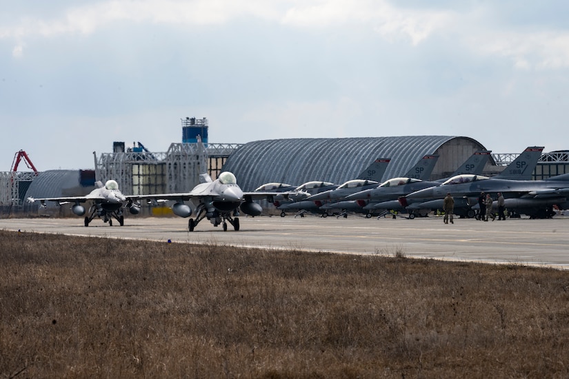 Aircraft taxi on a runway at a military air base.