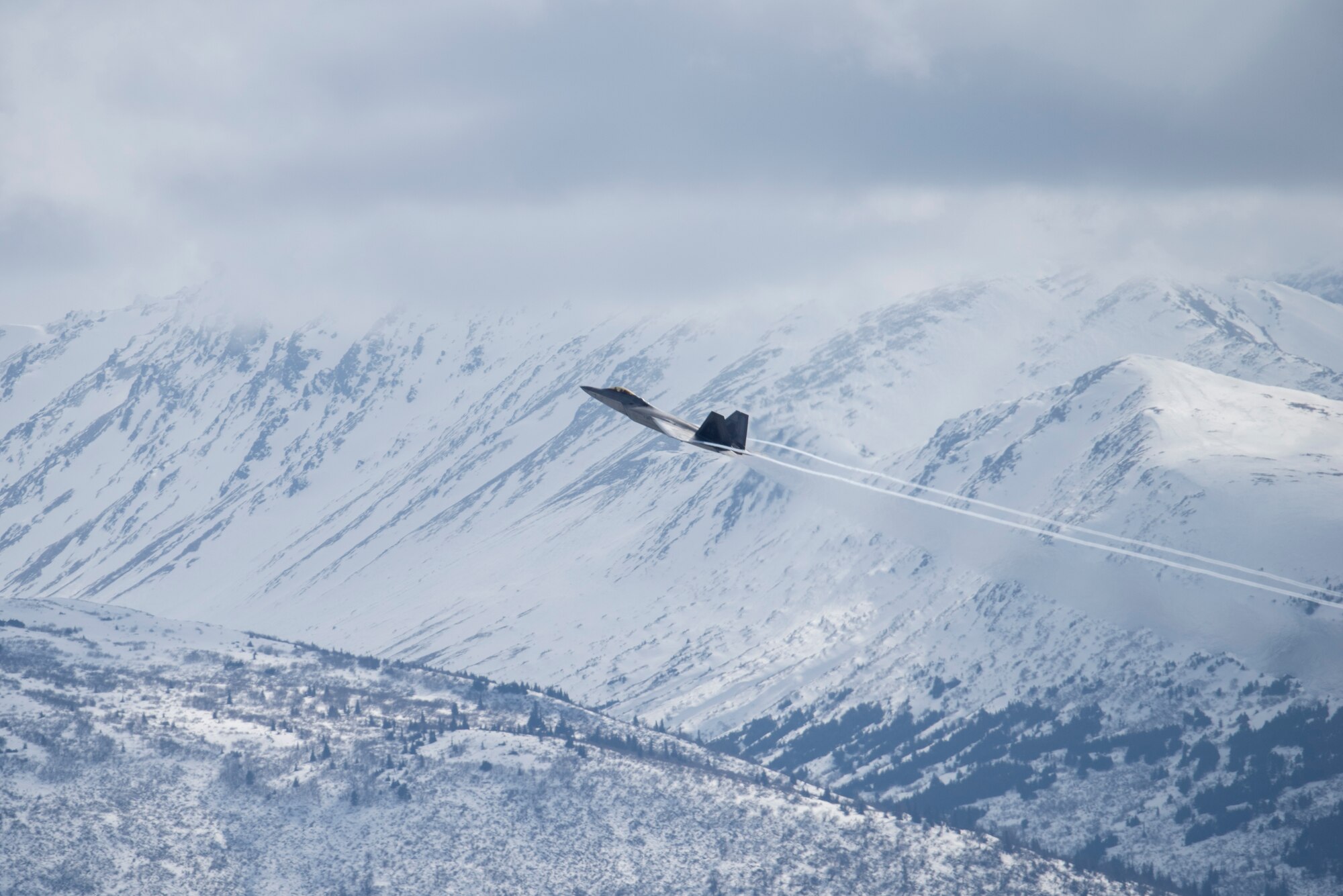 a fighter jet flies over mountains