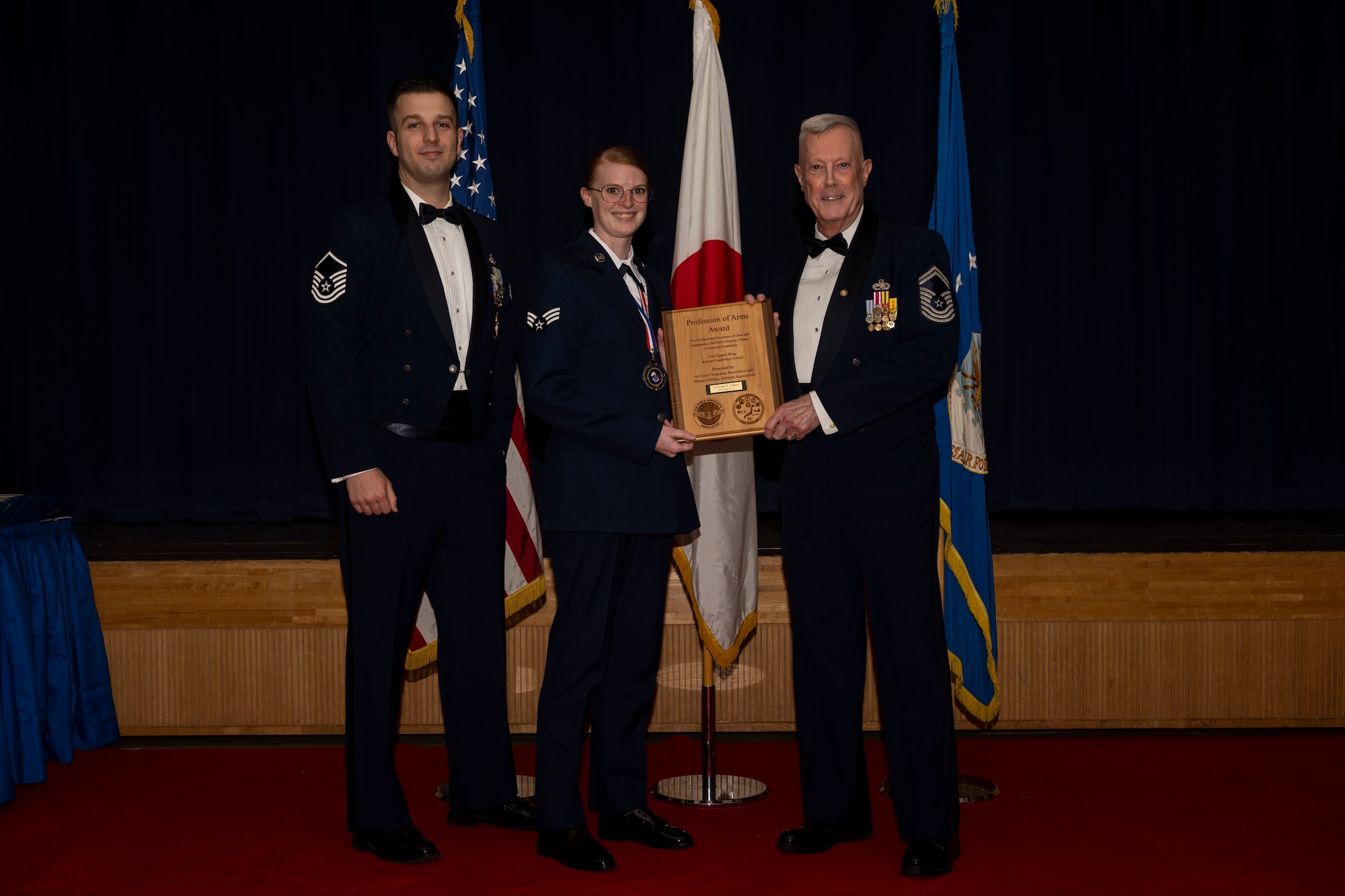 Group of military members in uniform pose for a photo holding an award.