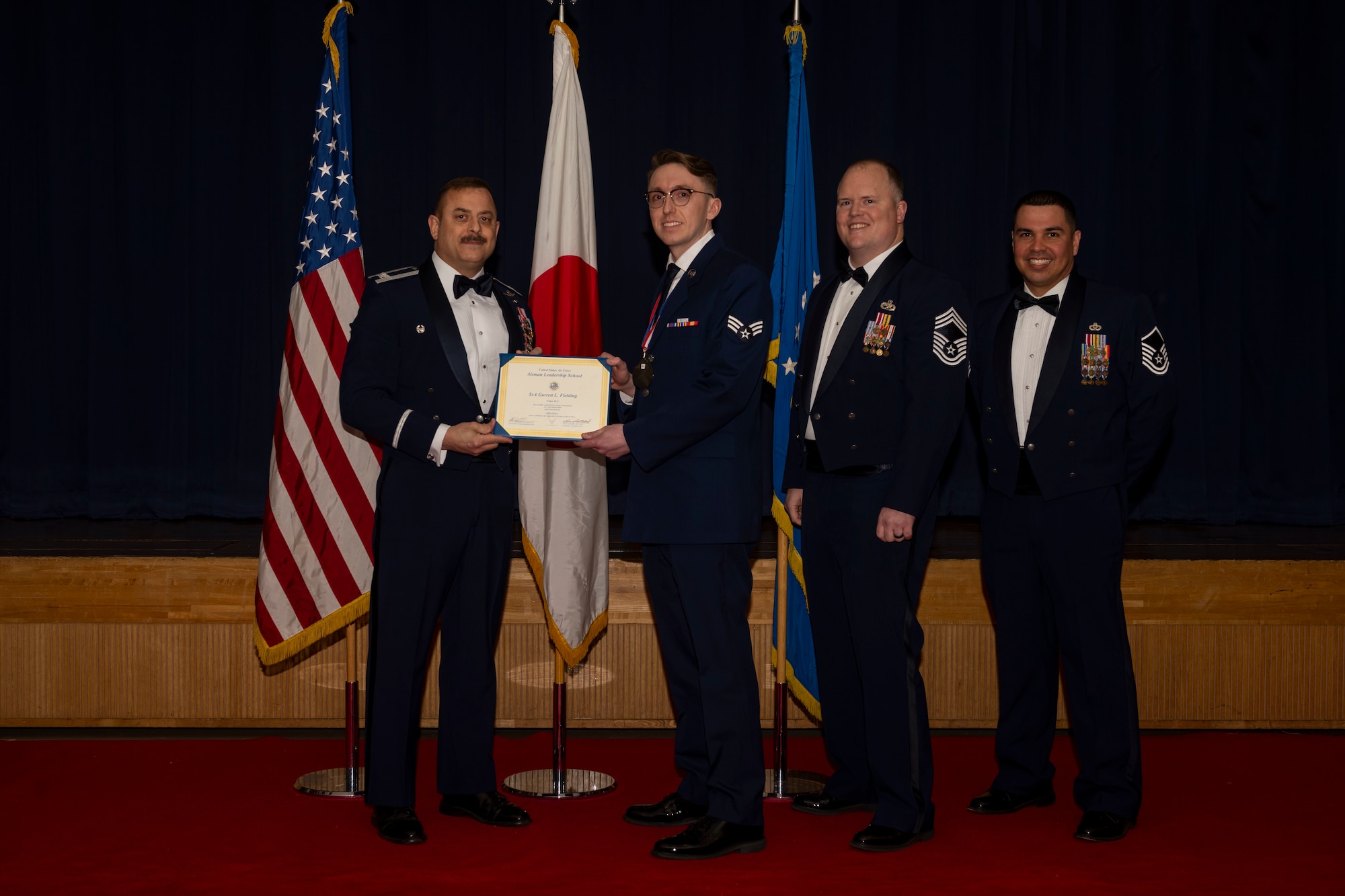 Group of military members in uniform pose for a photo holding a certificate.