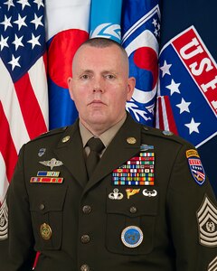 CSM Jcak H. Love in uniform standing in front of the following flags (from left to right): U.S. flag, South Korean flag, UNC flag, CFC flag, and USFK flag.