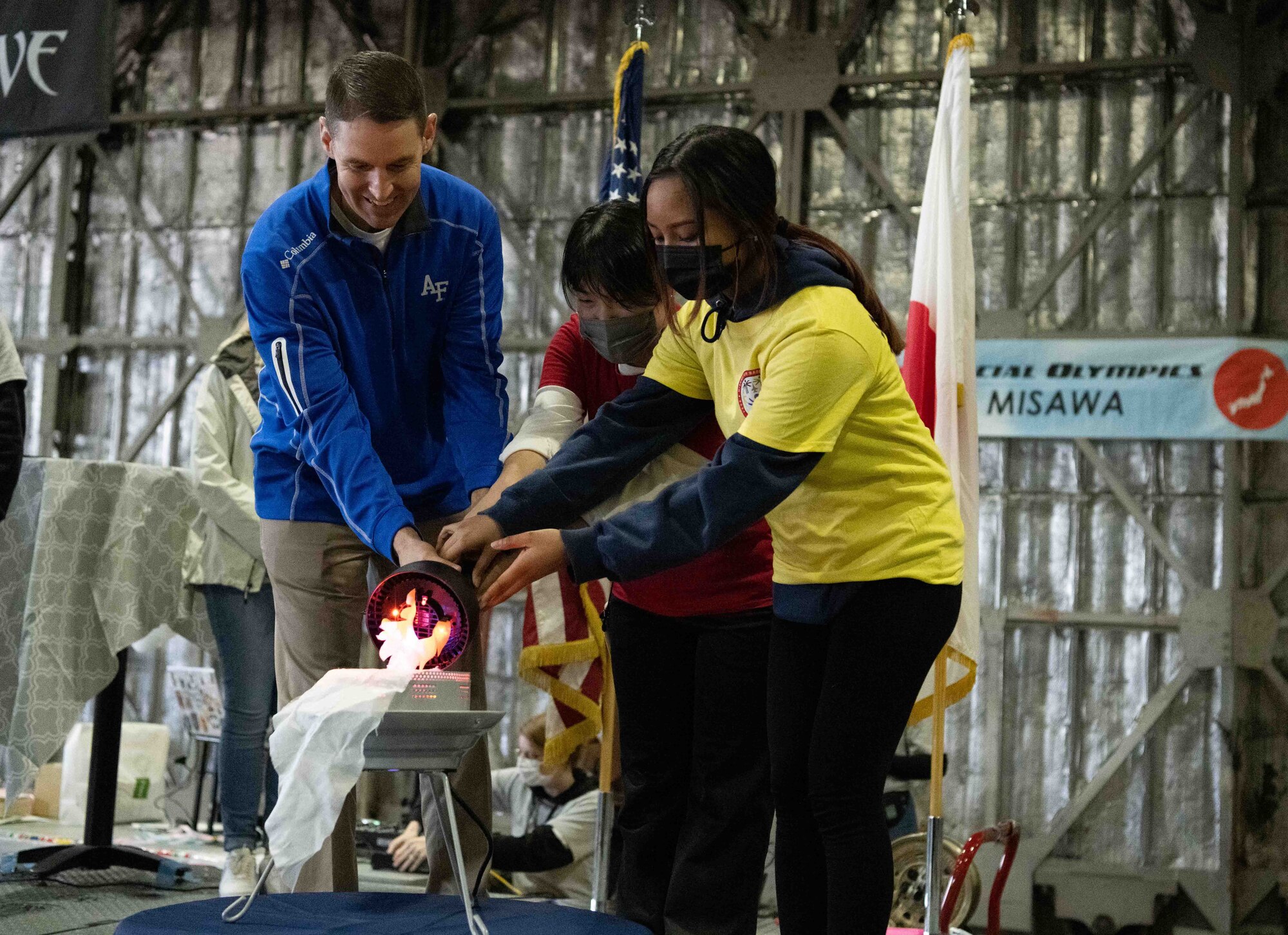 A military member, lights an electric flame lamp with an electric flame torch with an athlete and a participant.