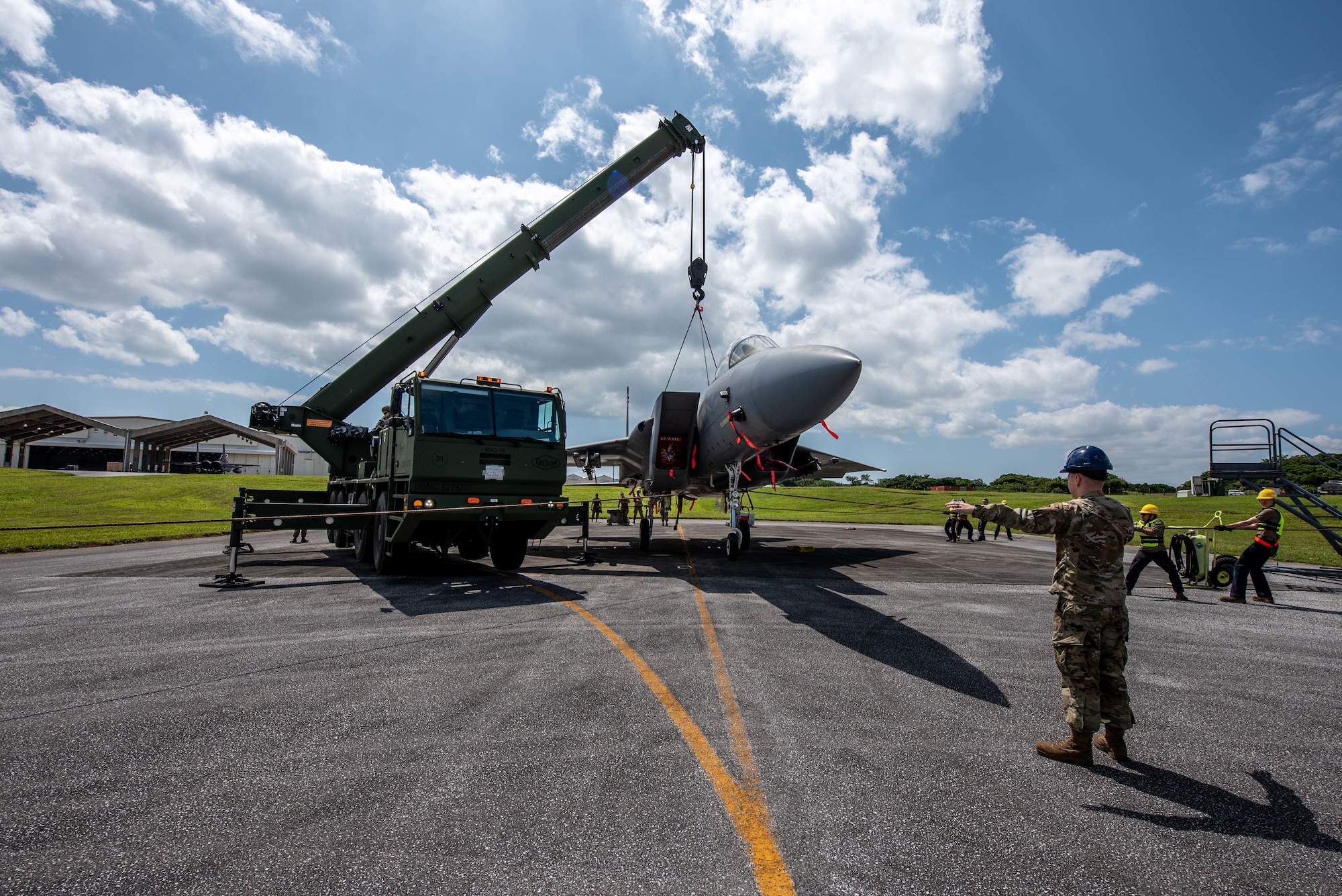 Airmen and Marines lift a plane with a crane.