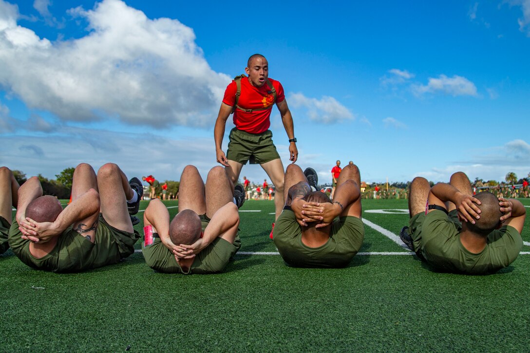 Marines do stomach crunches as a drill instructor stands above them.