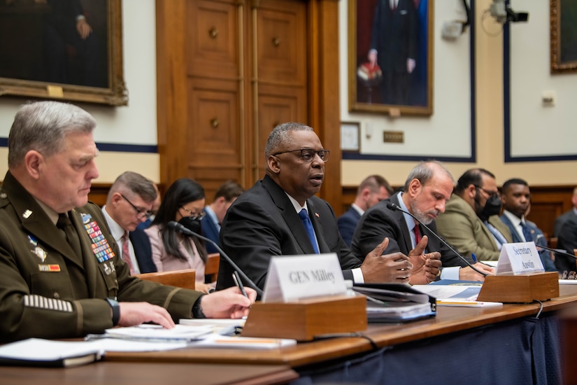 Joint Chiefs chairman, defense secretary and DOD comptroller sit at long table in front of audience.