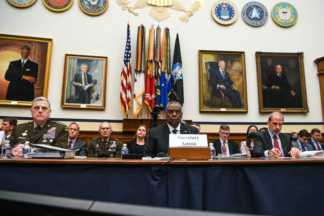 Joint Chiefs chairman, defense secretary and comptroller sit at long table.