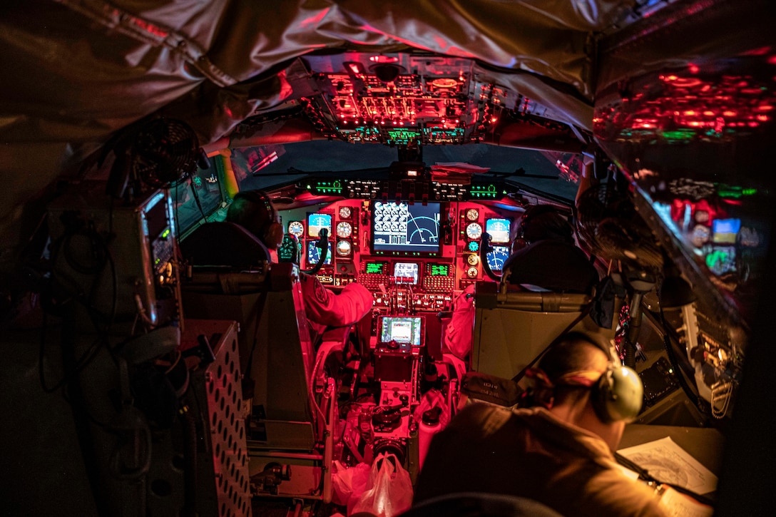 Airmen sit in the cockpit illuminated by red lights.