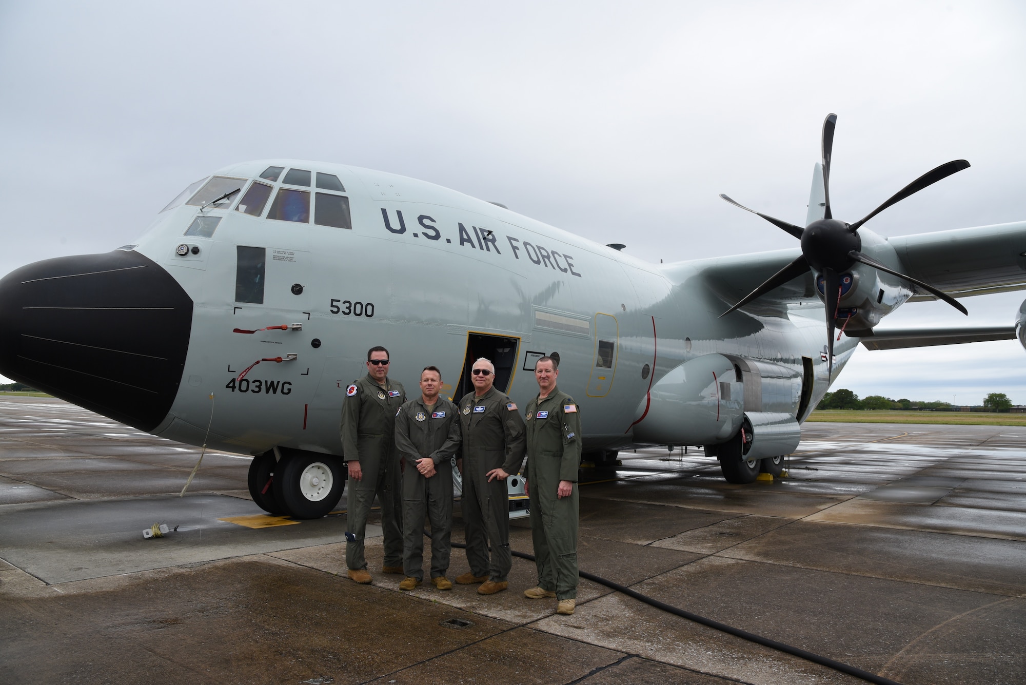four people stand next to WC-130J Super Hercules with a new, shiny gray paint scheme and vintage markings.