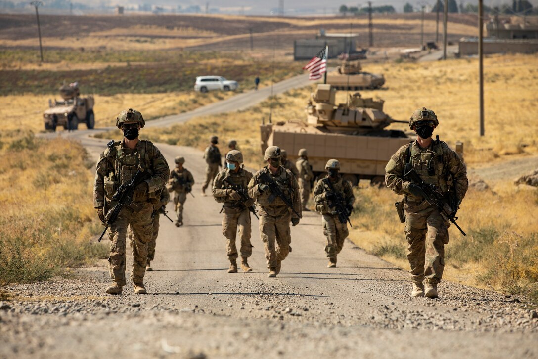 U.S. soldiers  walk up a dirt road Syria.