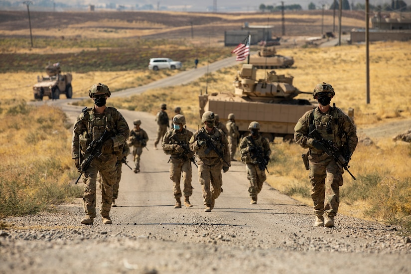 U.S. soldiers  walk up a dirt road Syria.