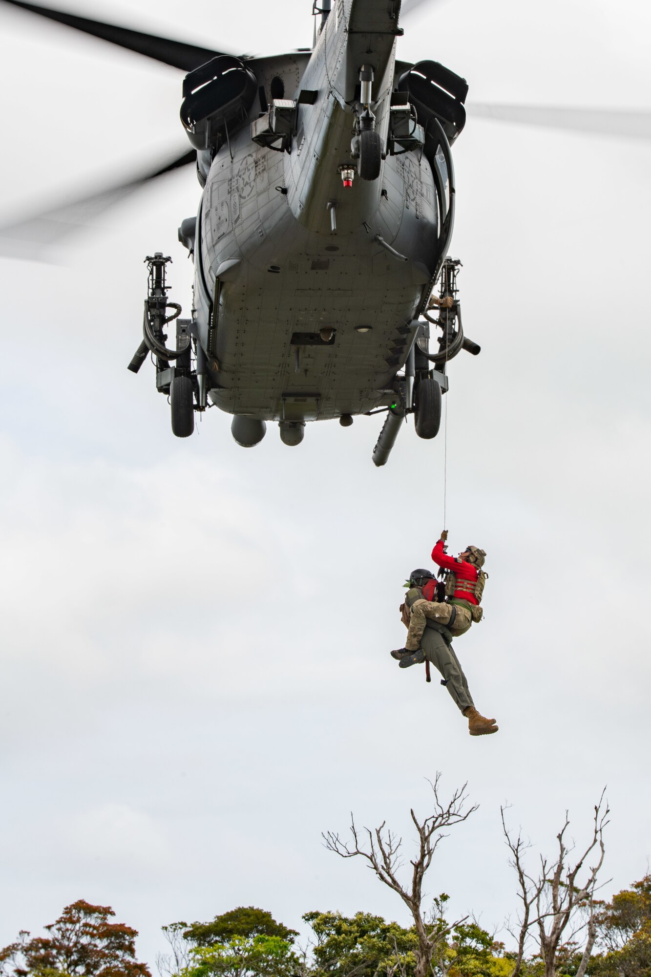 Two airmen get hosted up and out of the jungle into a helicopter