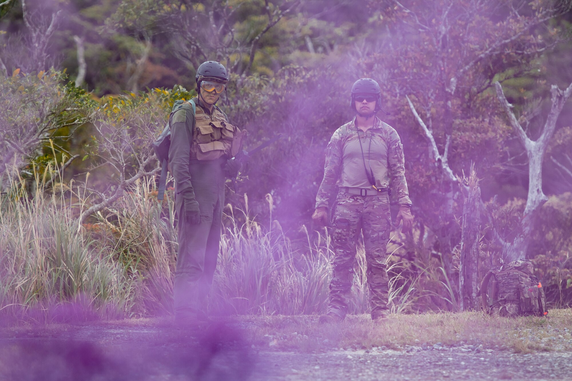 Purple smoke clouds the screen in front of two airmen waiting for a helicopter