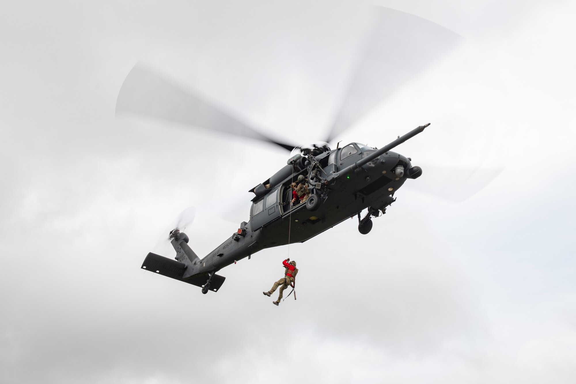 An airman hangs out of a helicopter