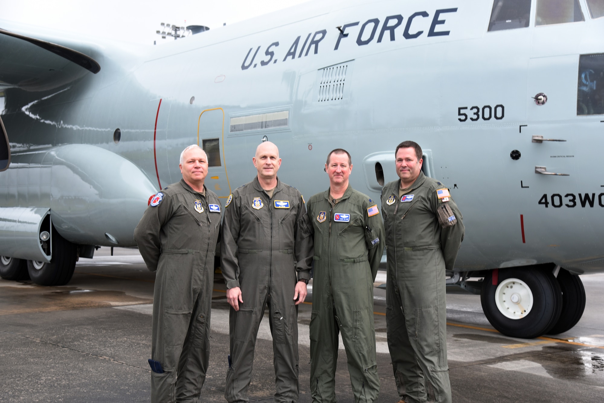 four people stand next to the new shiny gray painted WC-130J Super Hercules with vintage markings.