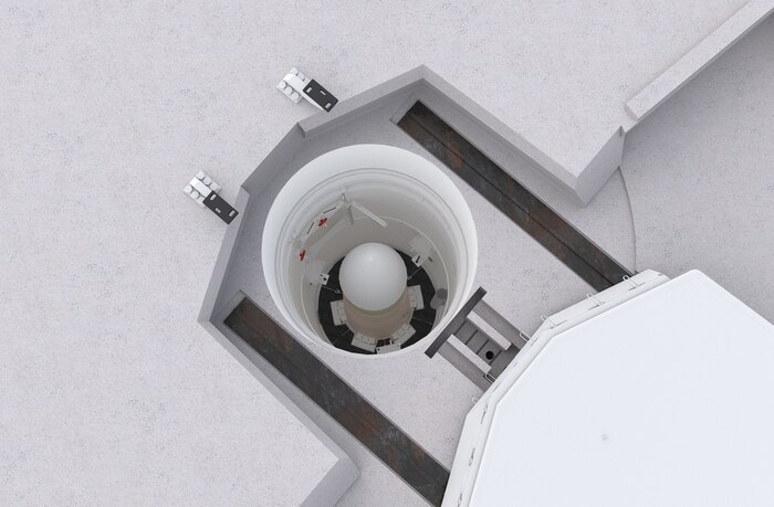 A man in a blue military jacket addresses a crowd in front of him.