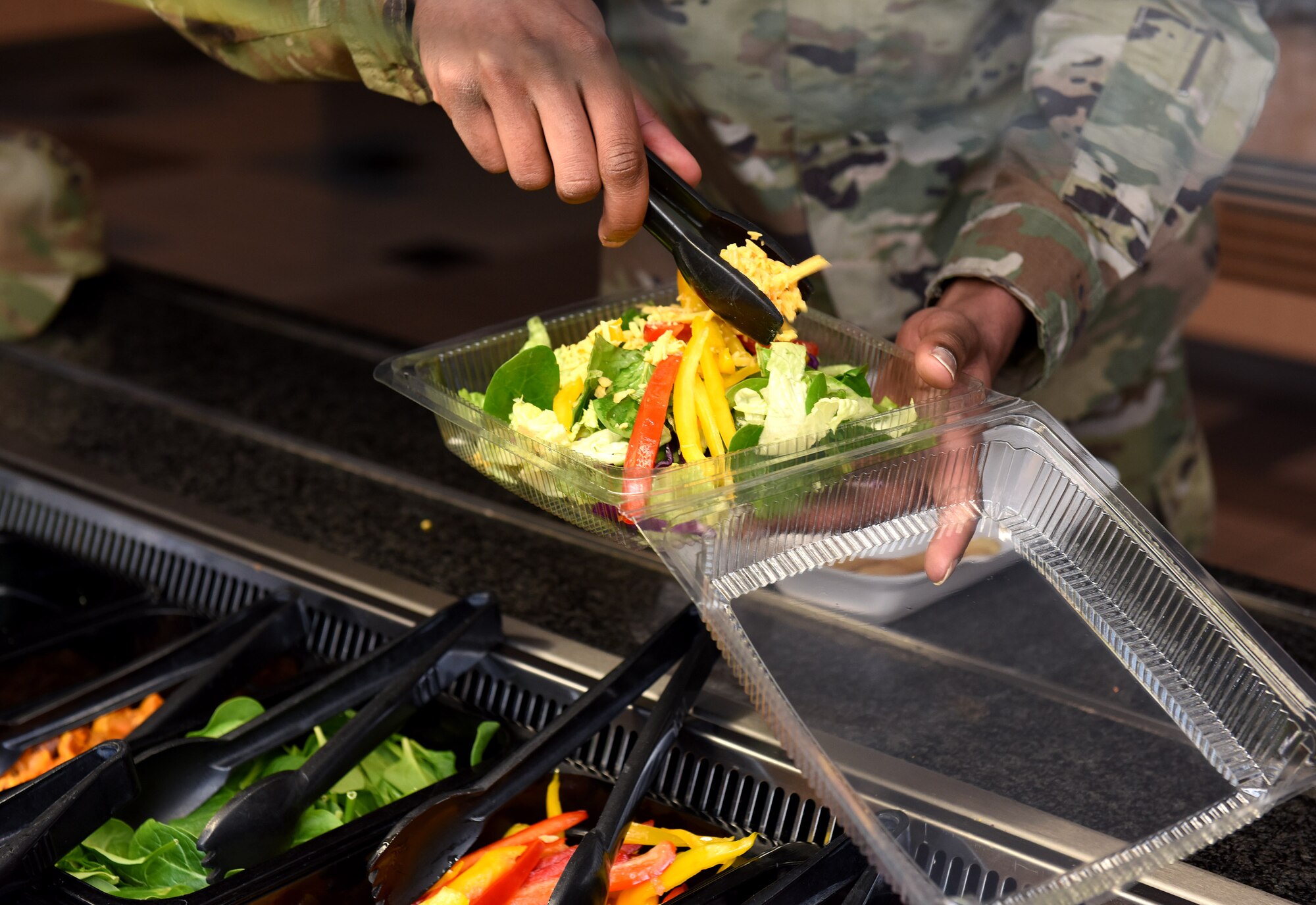 A customer at the Gateway Dining Facility fills a salad to-go box with a variety of fresh vegetables as part of his lunch at Royal Air Force Mildenhall, England, March 24, 2022. The DFAC provides a variety of different meal choices throughout the day for Team Mildenhall Airmen and civilians. (U.S. Air Force photo by Karen Abeyasekere)