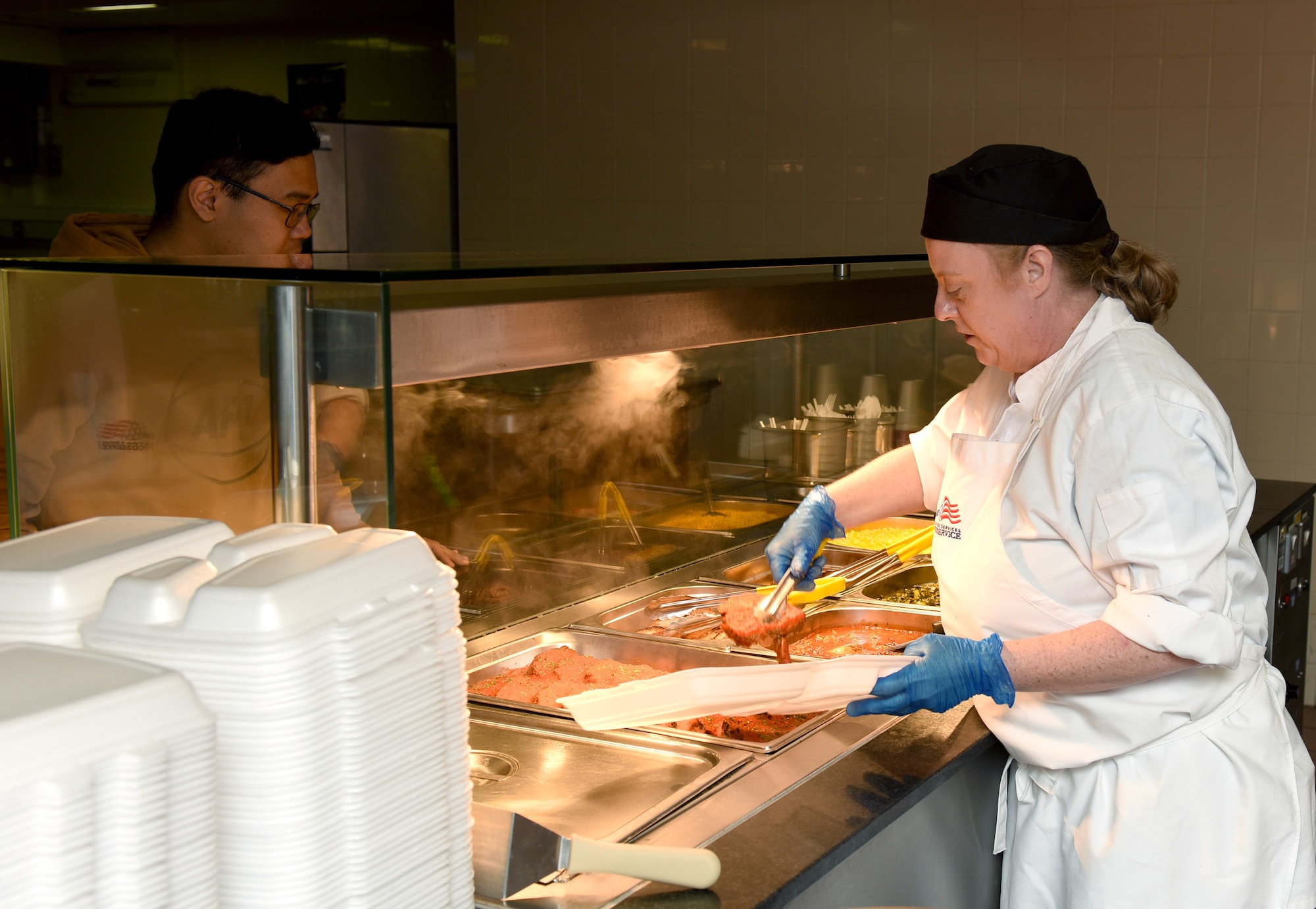 Tammy Halls, 100th Force Support Squadron Gateway Dining Facility cook, prepares and serves a hot meal to a customer at Royal Air Force Mildenhall, England, March 24, 2022. Staff work in different positions at the DFAC to give them an experience in a wide variety of duties. (U.S. Air Force photo by Karen Abeyasekere)
