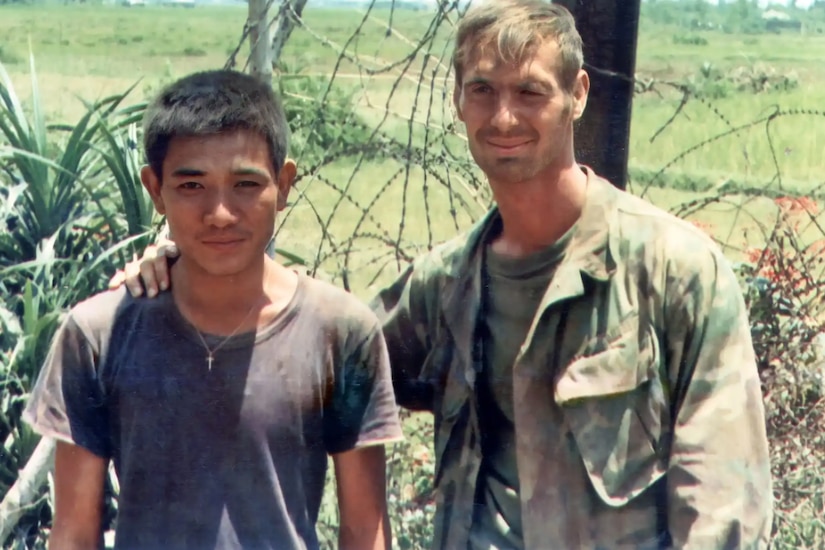 A man puts his arm around the shoulder of a younger man in a field.