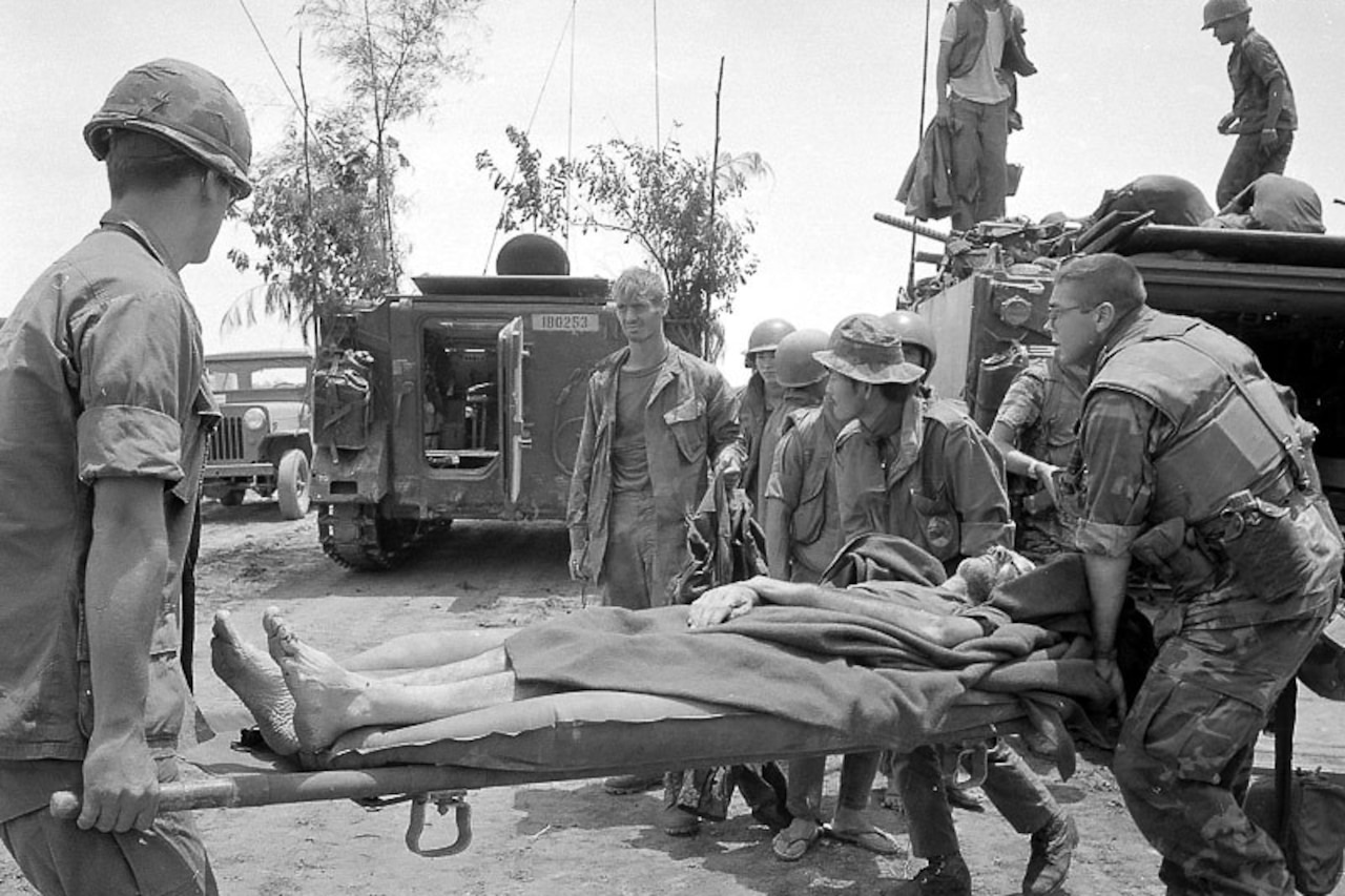 Several men stand around a stretcher as it’s taken to an armored vehicle.