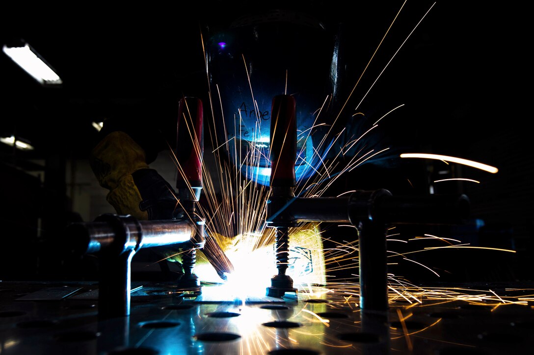 An airman wearing protective gear welds metal.