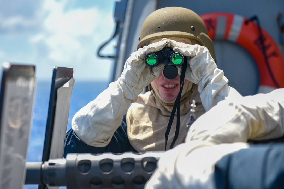 A sailor looks through binoculars.