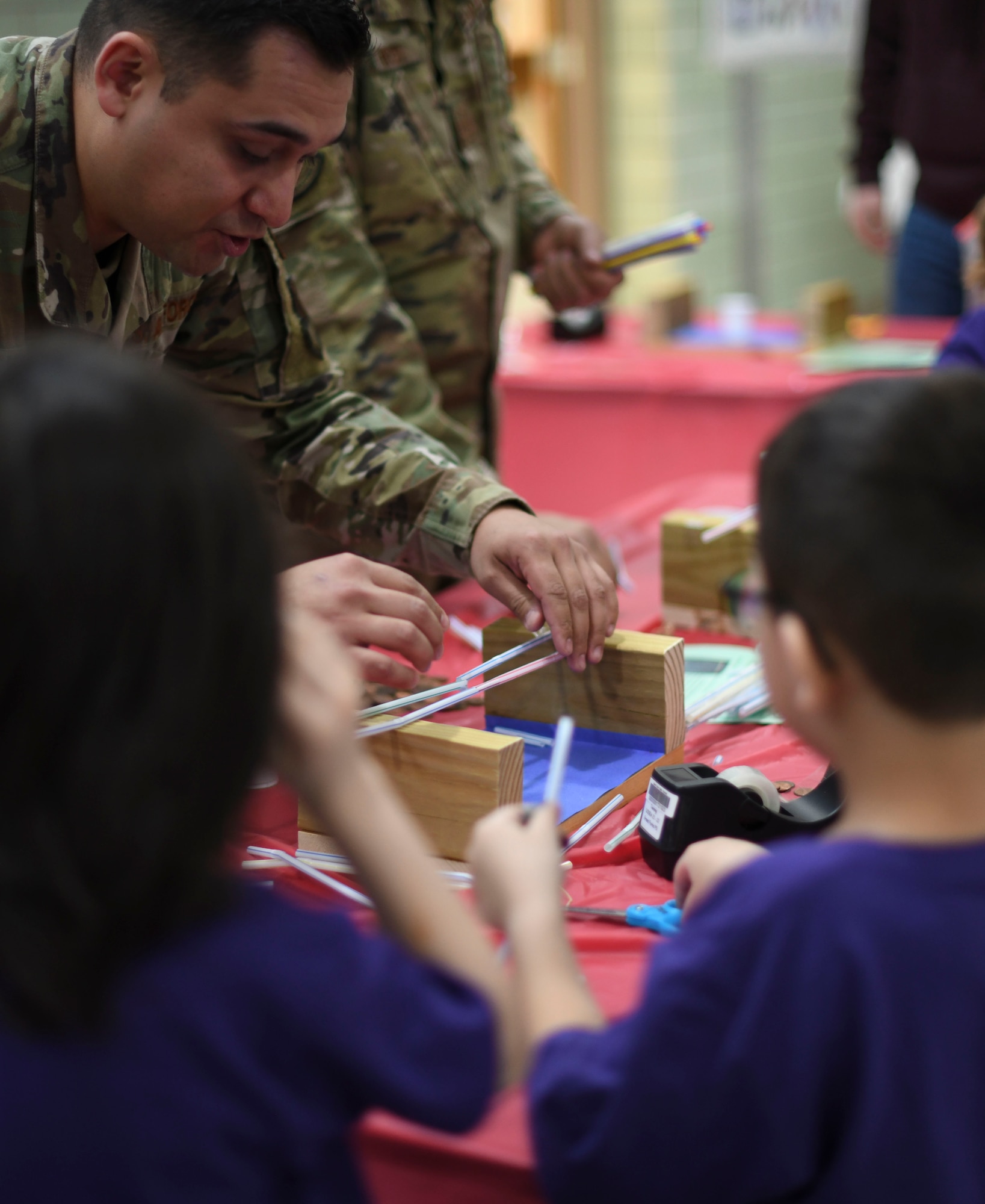 An Airman works with students to create a bridge out of straws.
