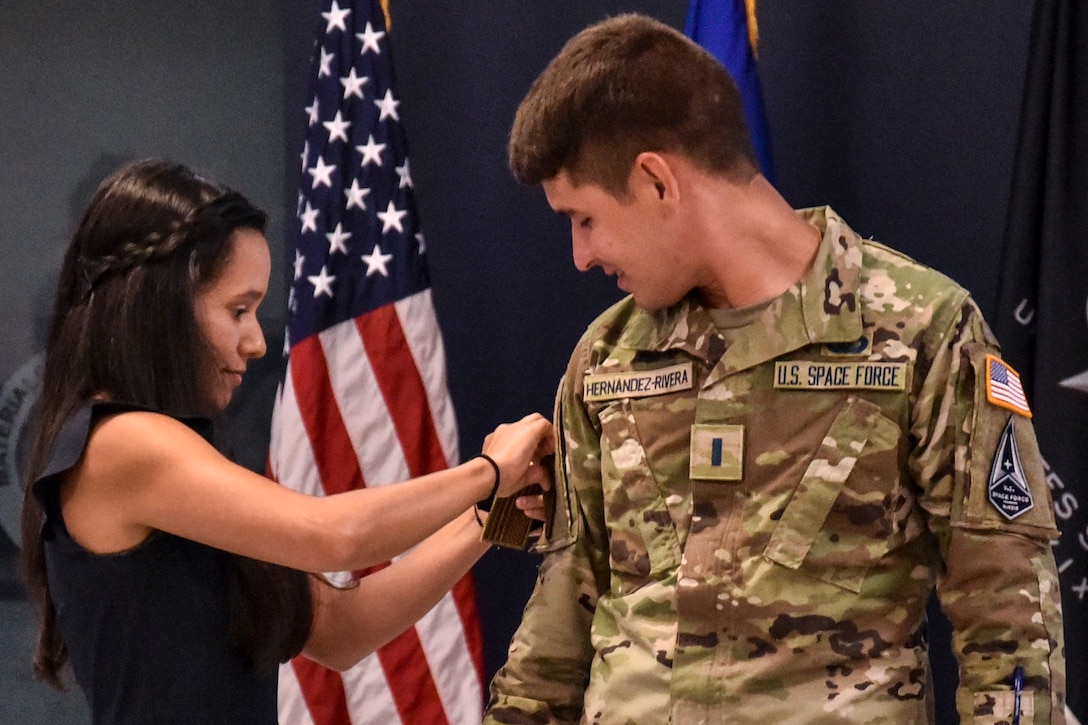 A woman places an insignia on the sleeve of a Guardian as he watches.