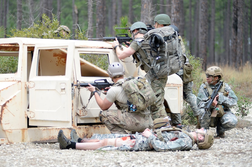 Service members with rifles seek shelter behind a disabled combat vehicle.