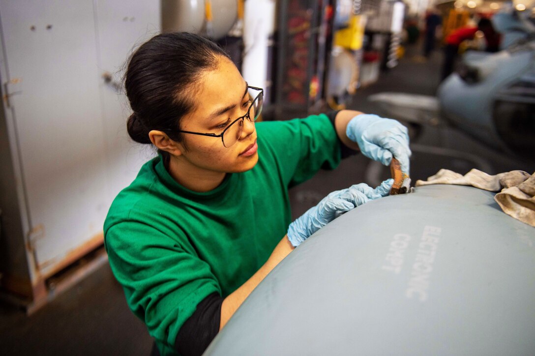 A sailor removes corrosion from a portion of aircraft.