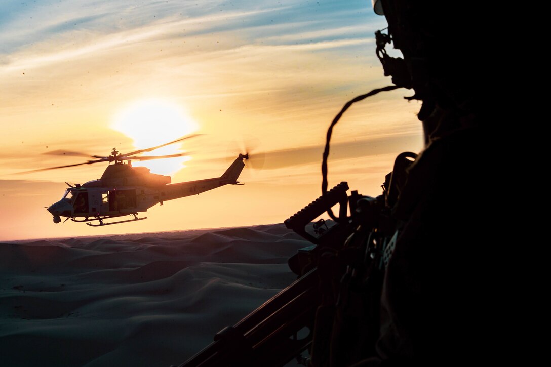 A helicopter is seen against a golden sky from the window of another aircraft.