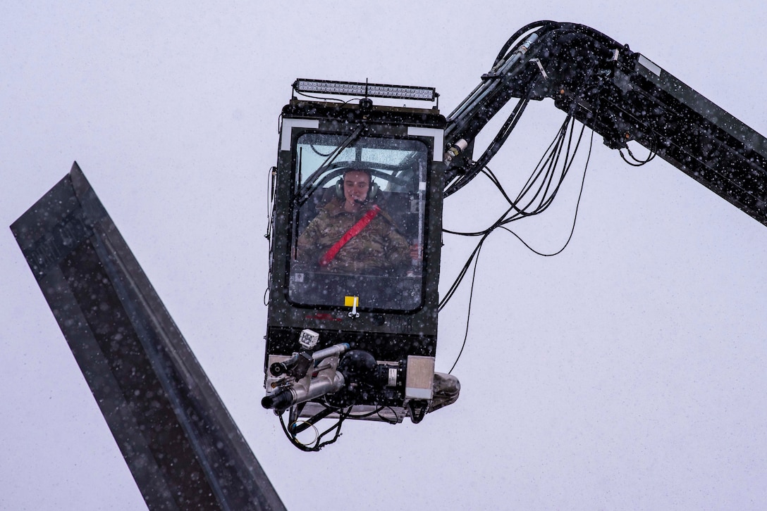 An airman rides in a small airborne  de-icing vehicle.