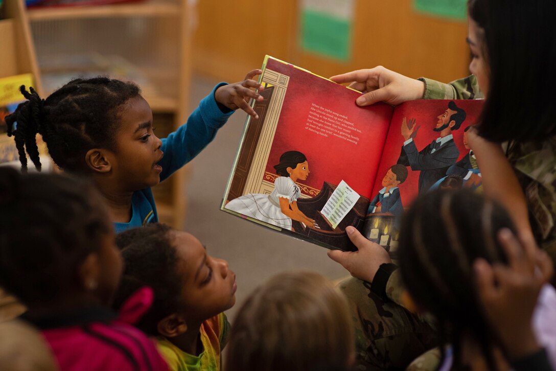 A group of children look and point to an open book.