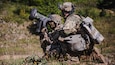 A servicemember kneels in a grassy area and operates military equipment.