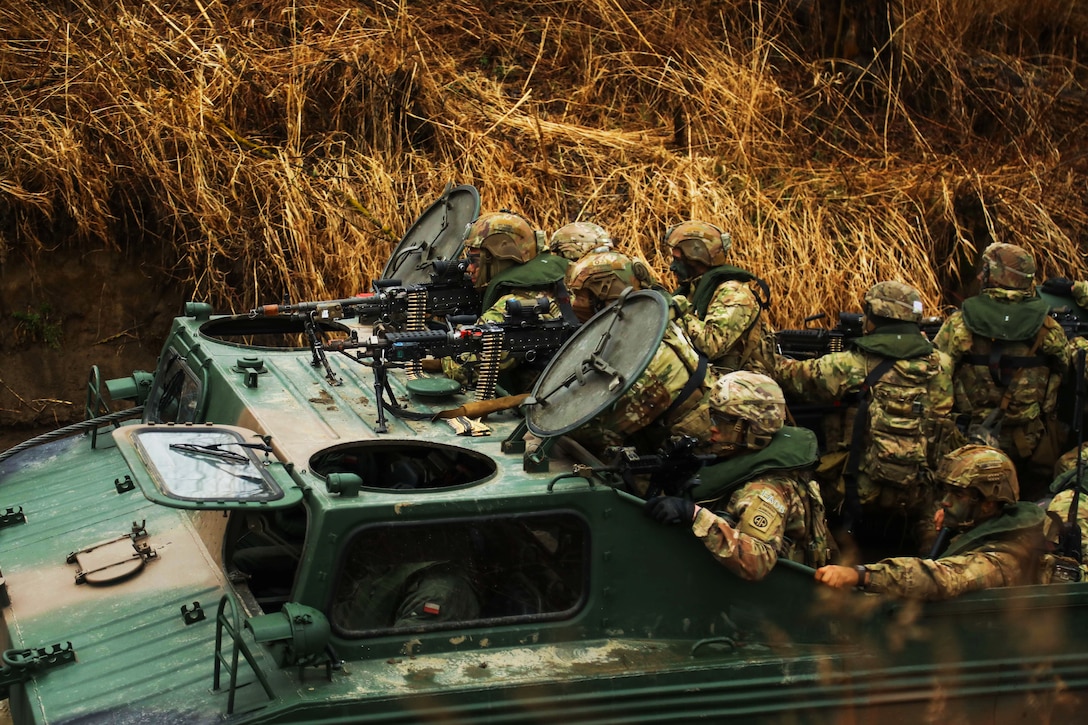 Soldiers hold weapons as they’re transported through a marshy area in the back of a military vehicle.