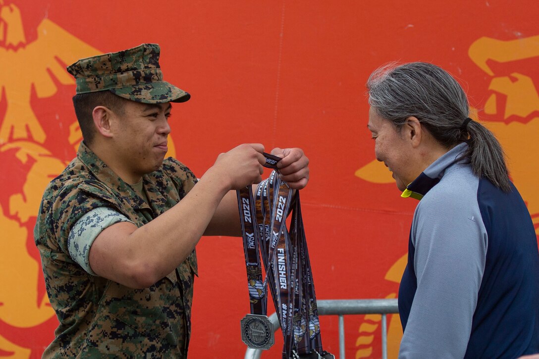 U.S. Marine Corps Staff Sgt. Bryan Reyes, accounting chief, Training Command, awards a runner with a medal for completing the Marine Corps Marathon 17.75k in Dumfries, Virginia, March 26, 2022. The event promotes physical fitness, generate goodwill in the community, and showcase the organizational skills of the Marine Corps. (U.S. Marine Corps photo by Cpl. Eric Huynh)