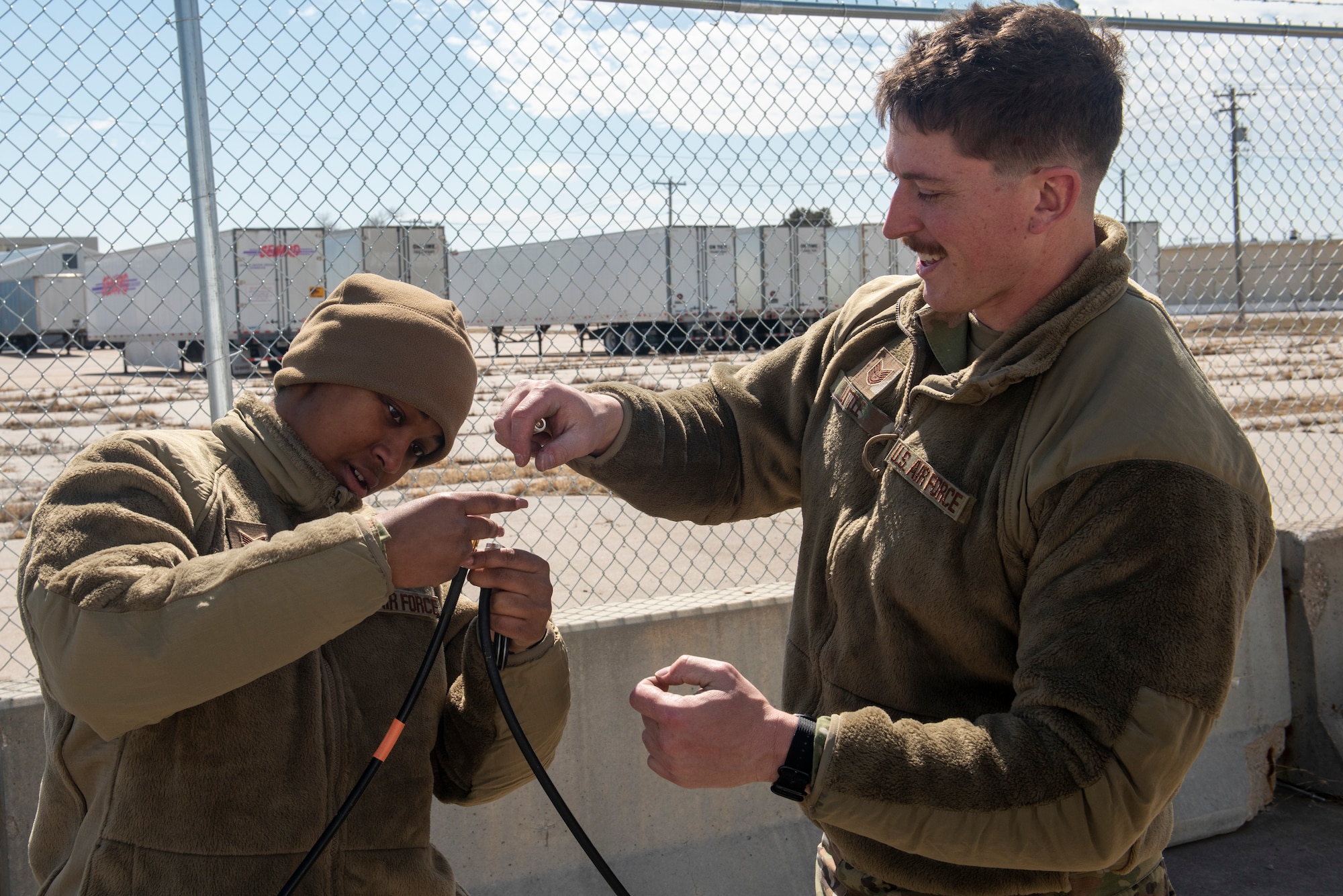 Two Airmen hold spliced cables as they attempt to connect them.