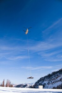 A Chinook helicopter sling loads a Black Hawk helicopter airframe.