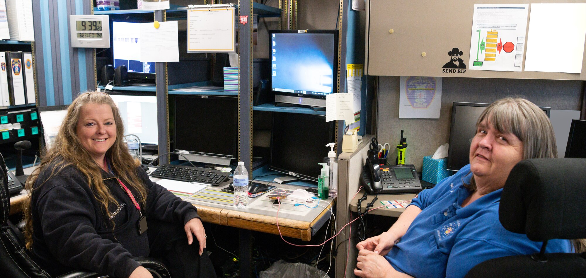 Mitsy Pickett, right, an Emergency Communications Center operator with Arnold Air Force Base Fire and Emergency Services, and Ginger Dyer, Emergency Communications Center coordinator, pose for a photo between calls and alarms, March 23, 2022, in the Emergency Communications Center at Arnold AFB, Tenn. (U.S. Air Force photo by Jill Pickett) (This image has been altered to obscure a badge and documents for security purposes.)