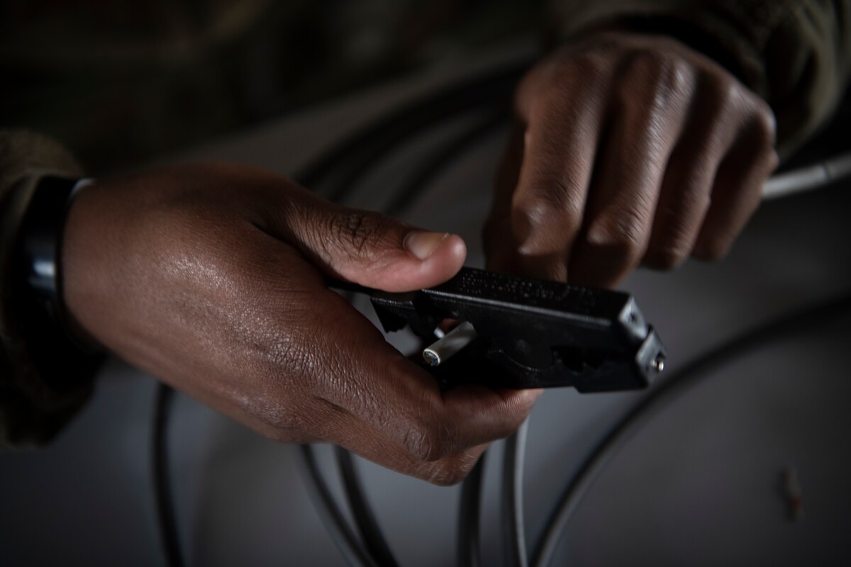 One hand holds a cable while a second cuts it.