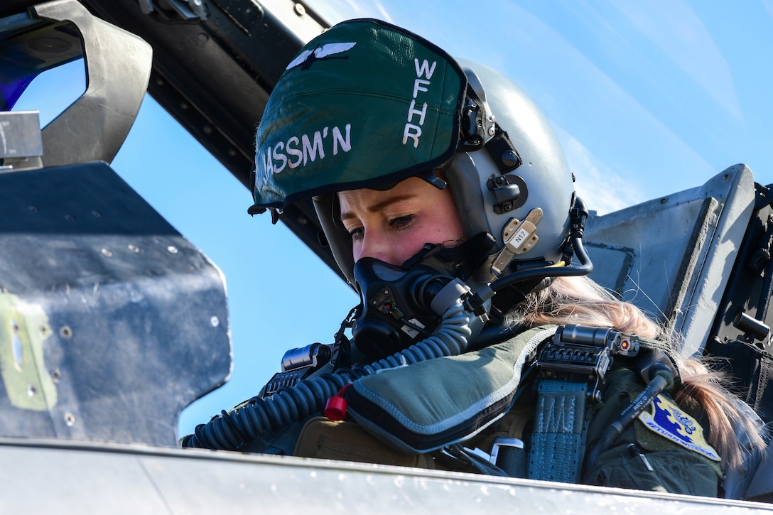 An airman sits in the cockpit of a jet to check flight controls.