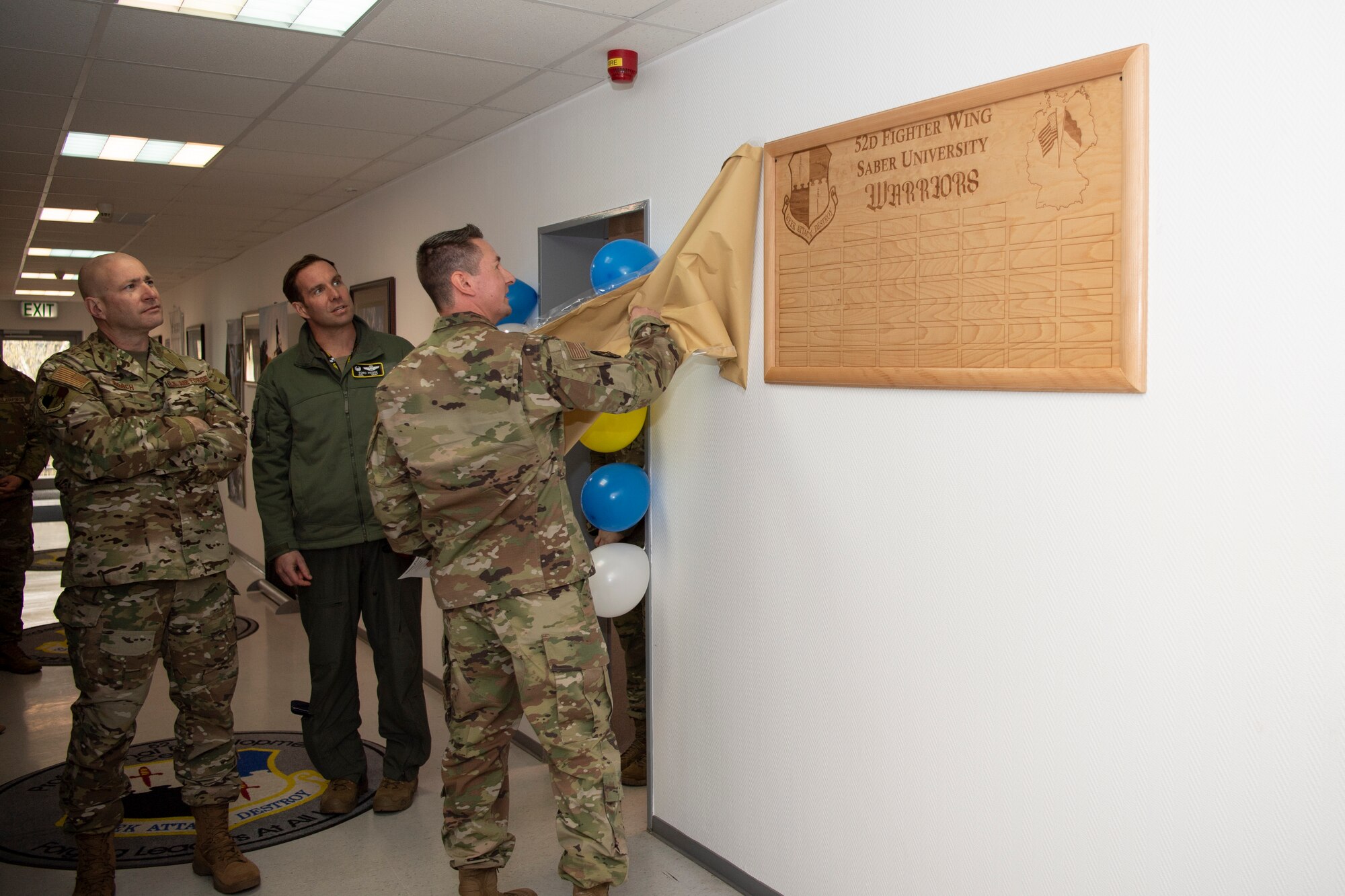 U.S. Air Force Senior Master Sgt. Chris Grube, 52nd Fighter Wing career assistance advisor, right, unveils a plaque for Saber University, Apr. 4, 2022, on Spangdahlem Air Base, Germany.