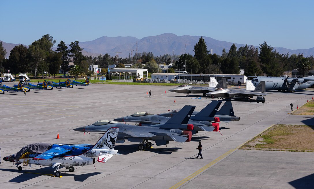 F-22 Raptors from the F-22 Demonstration Team out of Langley Air Force base wait on the hot ramp alongside a C-130J Super Hercules from the Texas Air National Guard and partner nation aircraft.