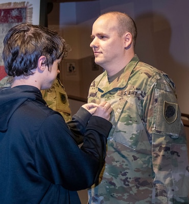 Alex Miller, son of newly promoted Chief Warrant Officer 4 David Miller, Jr., of Springfield, officer in charge of the automated and automation records branch, secures his new rank during a promotion ceremony at the Illinois State Military Museum in Springfield.