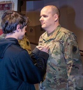 Alex Miller, son of newly promoted Chief Warrant Officer 4 David Miller, Jr., of Springfield, officer in charge of the automated and automation records branch, secures his new rank during a promotion ceremony at the Illinois State Military Museum in Springfield.