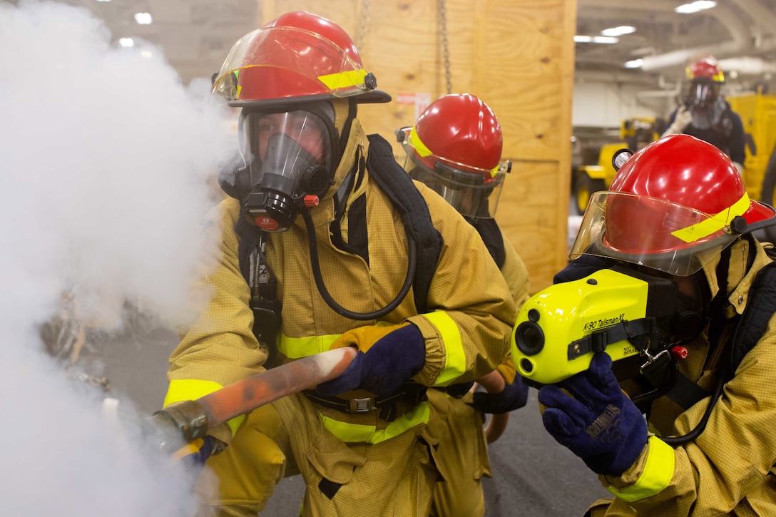 Sailors in firefighting gear work to put out a simulated fire.