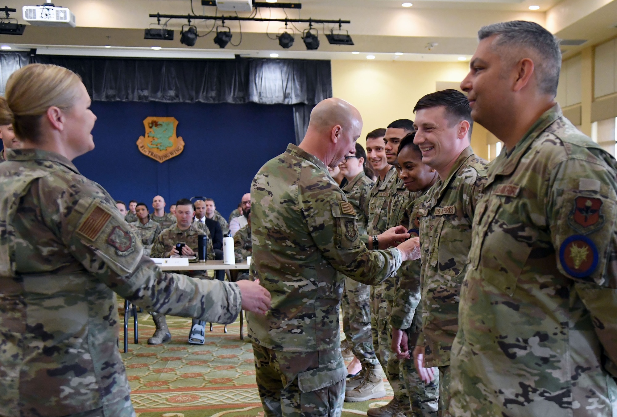 U.S. Air Force Col. William Hunter, 81st Training Wing commander, provides patches to Keesler's first Dragon University Airmen as Chief Master Sgt. Sarah Esparza, 81st Training Wing command chief, shakes their hands inside the Bay Breeze Event Center at Keesler Air Force Base, Mississippi, April 6, 2022. Dragon University is the 81st Training Wing's Professional Development Incentive Program. The program is led by the Keesler Air Force Base career assistance advisor, and is supported by the Total Force Development Council, Chief's Group, Company Grade Officer Council, Top III and the 5/6. After completing the program, each Airman will receive a patch for military members and a pin for civilians. (U.S. Air Force photo by Kemberly Groue)