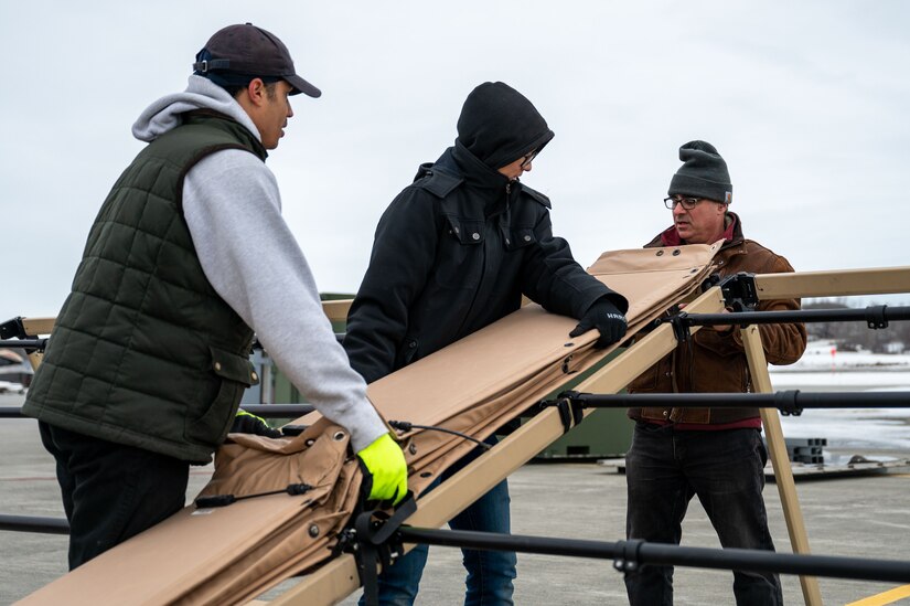 A photo of three people unrolling a sheet of solar panels